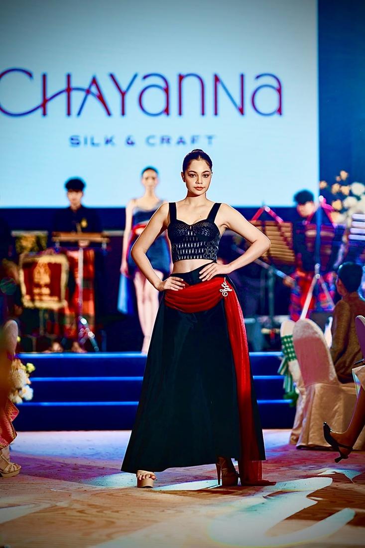 Model on the runway in a black corset top and long black skirt with a red sash